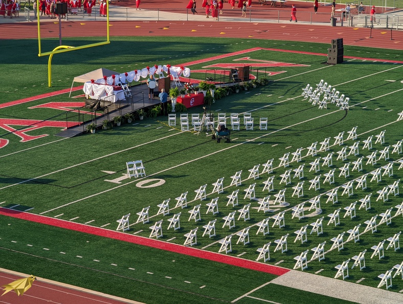 Graduation stage with podium and rows of white folding chairs on a football field