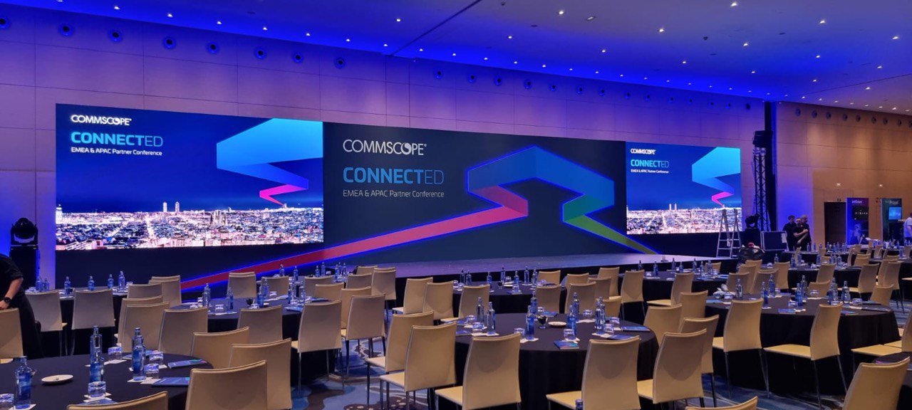 Corporate conference ballroom with large video screens and stage lighting.