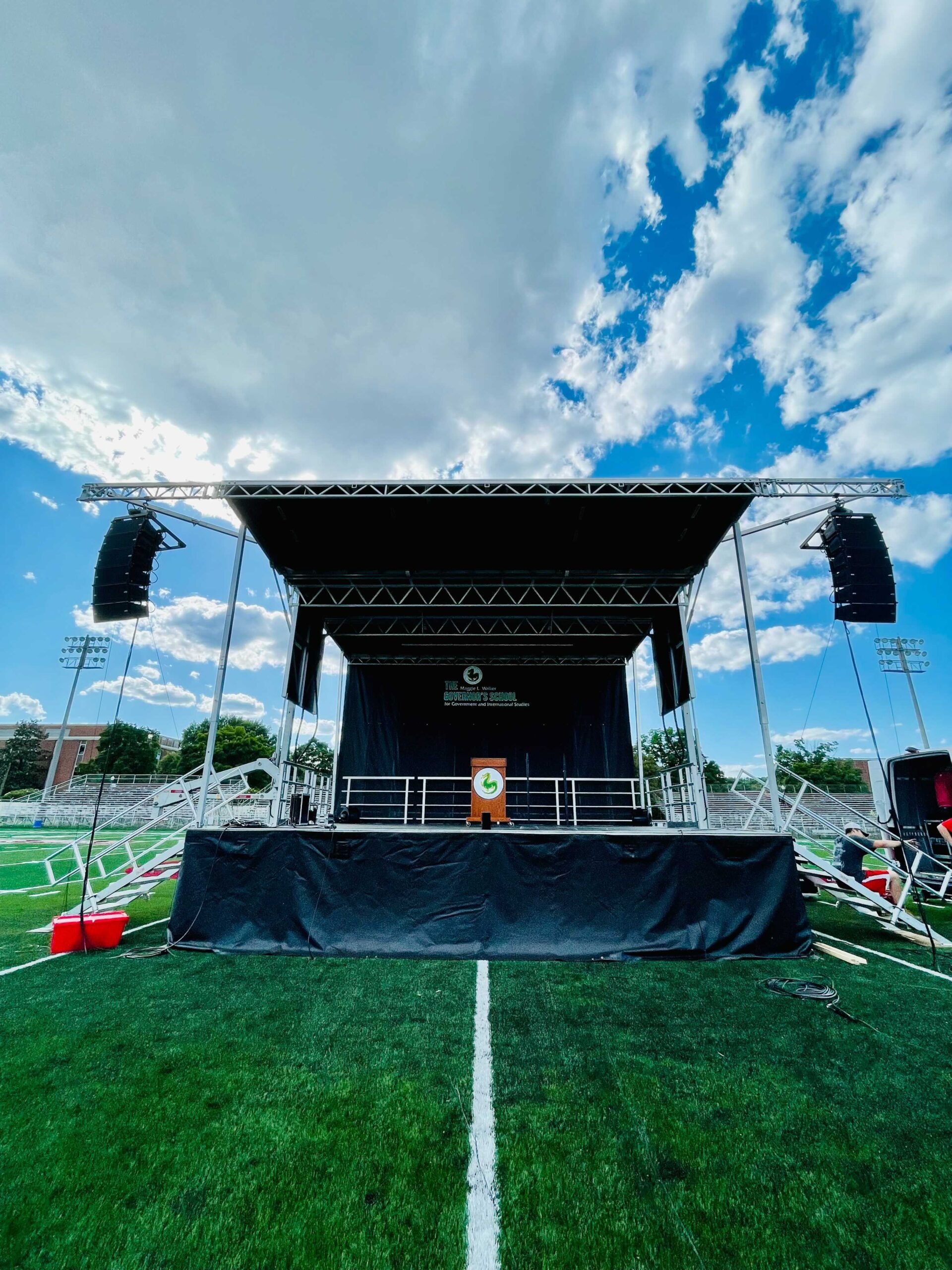 Graduation ceremony stage with a PA speaker system and overhead rigging on a school field