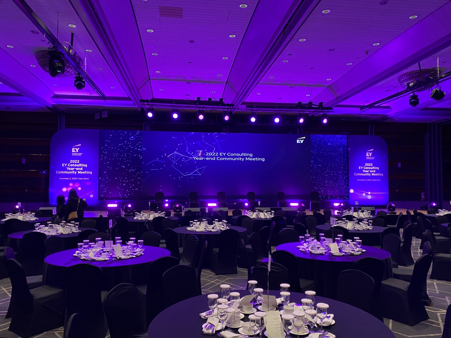 Corporate stage with overhead purple lighting fixtures and an LED backdrop in a ballroom