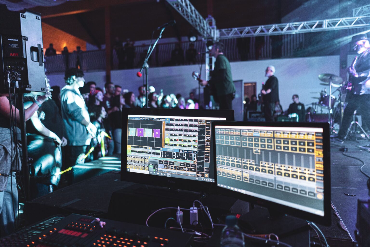 Live band performing under stage lighting, with audio production equipment visible in the foreground.